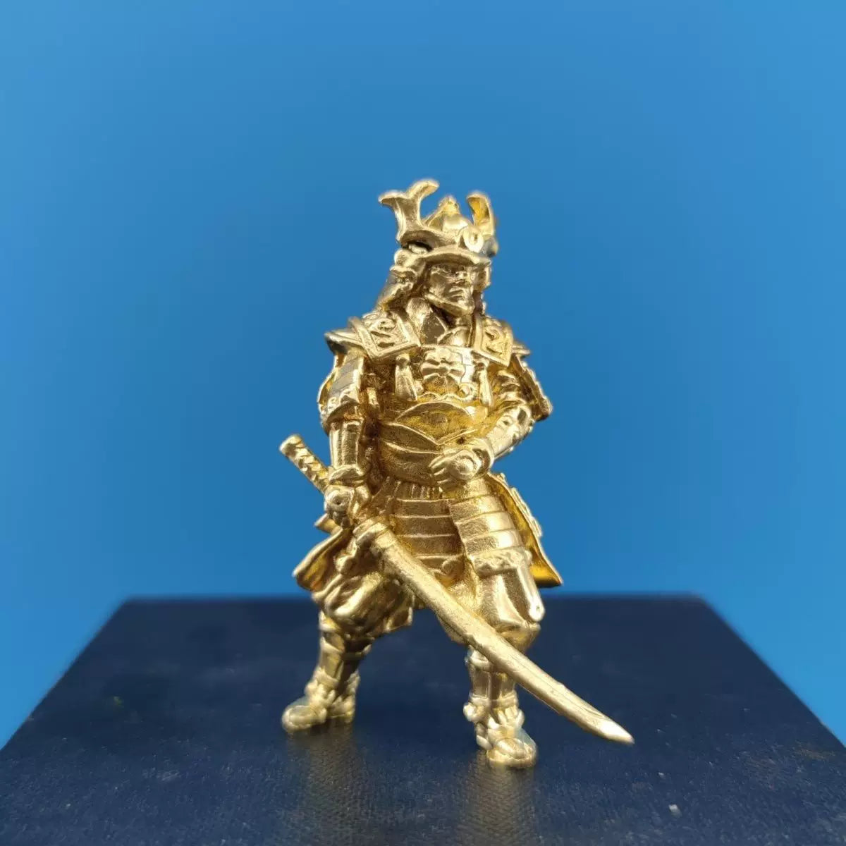 Solid brass samurai figurine with drawn sword, shown beside a coin for scale